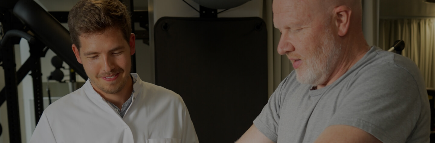 Physical therapist assisting an older man with arm exercises in a gym setting