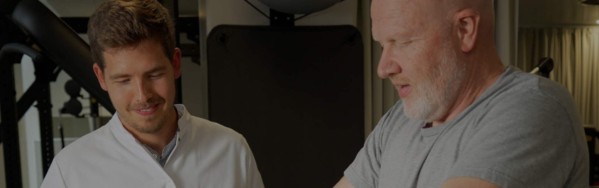 Physical therapist assisting an older man with arm exercises in a gym setting